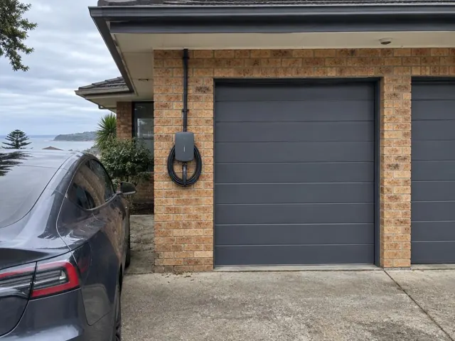 Wall-mounted EV charger beside a garage door on a brick home in Narrabeen