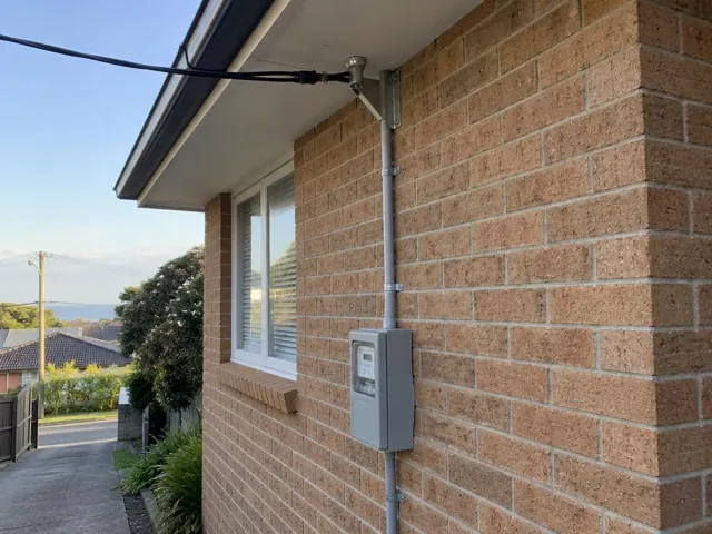 Overhead service cable and point-of-attachment bracket on a brick house exterior in Collaroy